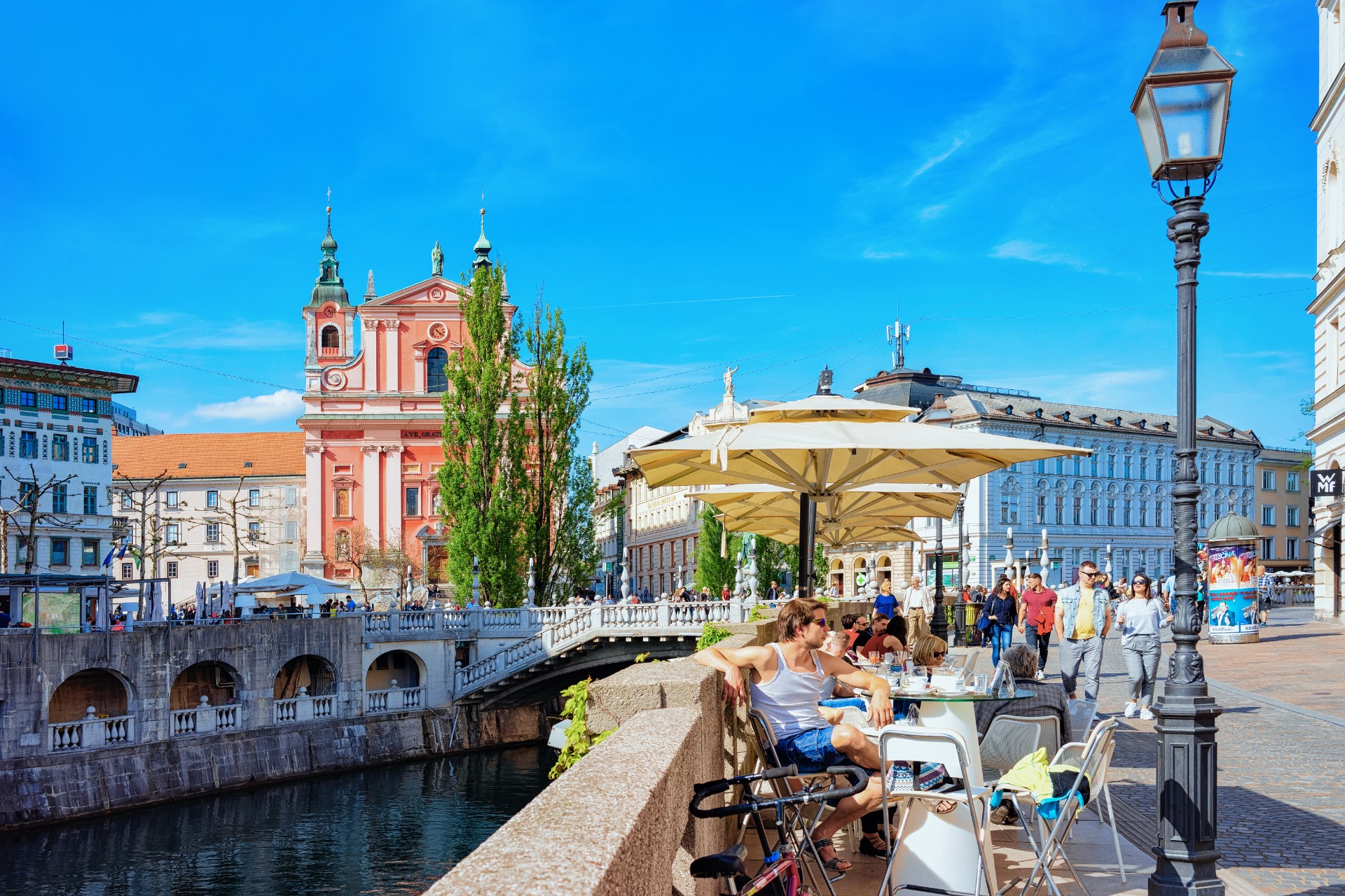 Lidé v kavárně na Trojmostí u řeky Ljubljanice v Lublani